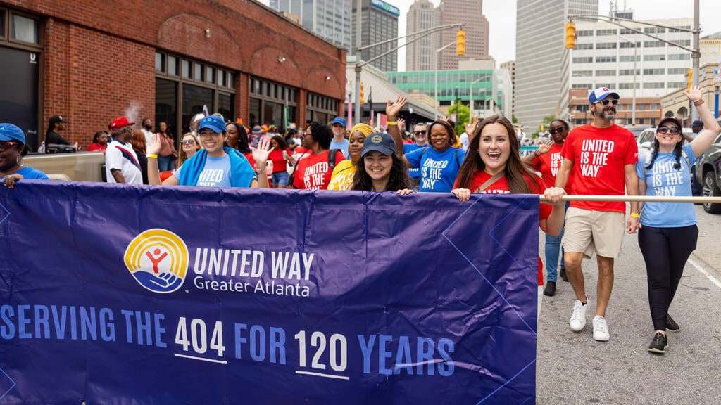 A group of volunteers and staff wearing Atlanta shirts and United is the Way shirts hold a parade banner.