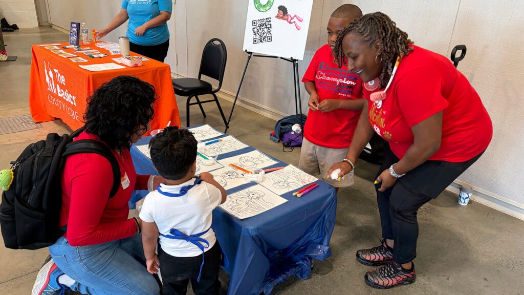 A volunteer and her son lead a coloring activity for a family in their community at a tabling event.