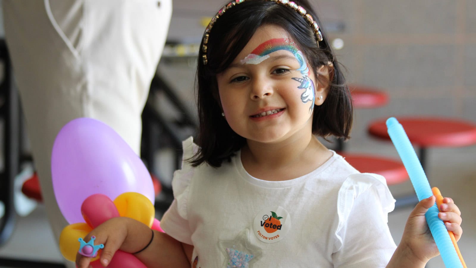 Young girl at a summer youth program holding colorful balloon creations with face paint
