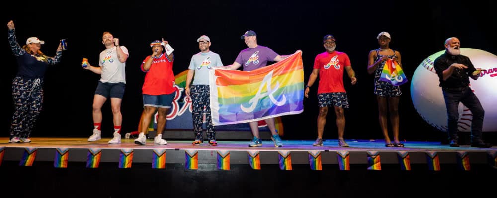 A line of Pride Night attendees dance and hold out Pride flags emblazoned with the Atlanta Braves logo.