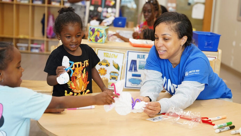 A United Way of Greater Atlanta volunteer makes a craft project with two young students in a classroom.