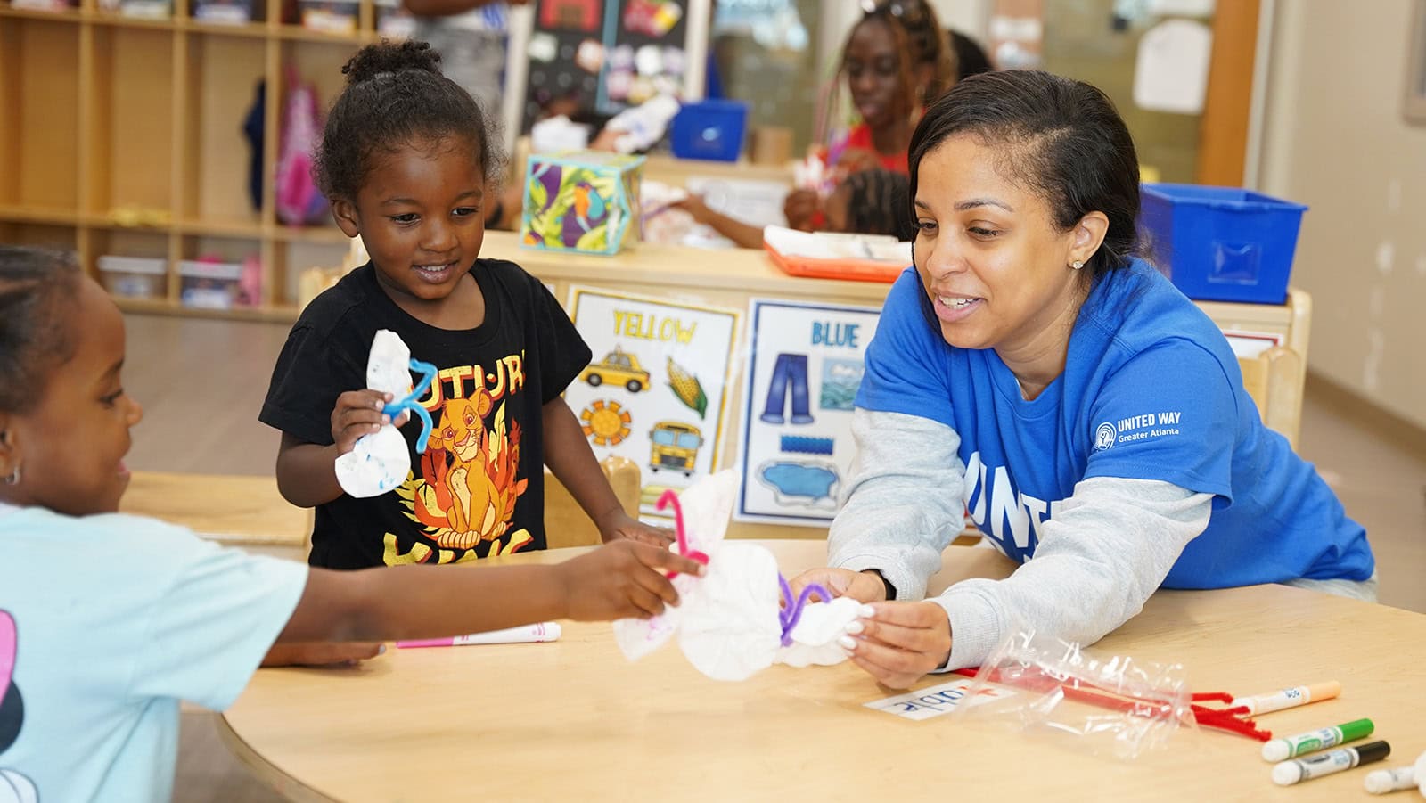 A United Way of Greater Atlanta volunteer makes a craft project with two young students in a classroom.