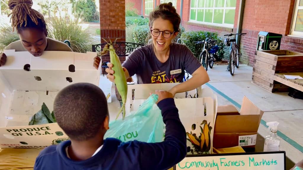 Farmer’s Market volunteer hands fresh corn to a student as part of a creative United Way “SNAP gap” reduction program in Atlanta